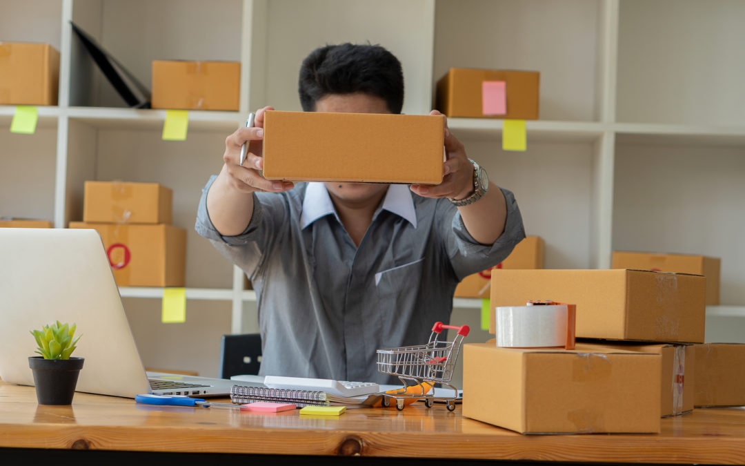 Man holding a box above a desk containing a laptop and mini shopping cart.